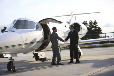 Businessmen shake hands by corporate jet
