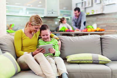 Family at home. Focus is on foreground, on a happy mother and son sitting on sofa and using digital tablet.
