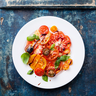 Ripe fresh colorful tomatoes salad with olive oil and balsamic vinegar on blue wooden background