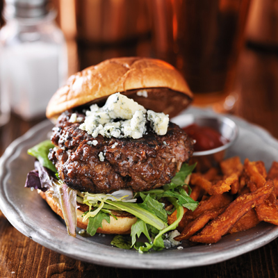 gourmet burger with blue cheese and sweet potato fries on metal plate.